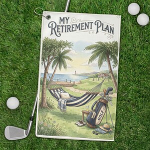 May include: Golf towel with a scenic illustration of a coastal golf course, a hammock, and the text "MY RETIREMENT PLAN." The towel is on green grass with golf balls and a golf club.