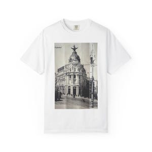 May include: White t-shirt featuring a black and white image of a building with a domed roof and a statue on top. The word "Español" is printed on the image. The shirt has a crew neck and short sleeves.