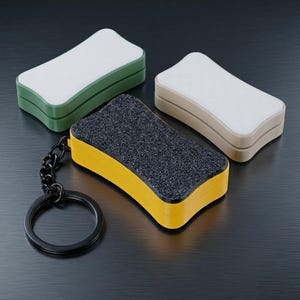 Op de afbeelding: Drie rechthoekige gummen in groen, beige en geel. De gele gum heeft een zwart, getextureerd oppervlak en een zwarte sleutelhanger. De andere twee gummen hebben witte oppervlakken. De gummen zijn ontworpen om schoon te maken.