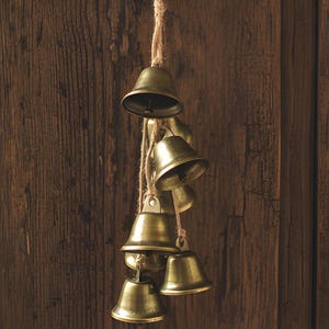 May include: A rustic door knocker featuring a wooden ring and a cluster of small brass bells hanging from a rope. The door is made of dark brown wood with visible grain and a brass doorknob.