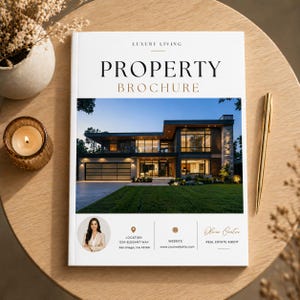 Op de afbeelding: Een witte vastgoedbrochure met de titel "PROPERTY BROCHURE" en de woorden "LUXURY LIVING" bovenaan. De brochure toont een modern huis met een groen gazon. Een gouden pen en een brandende kaars liggen op een houten tafel.