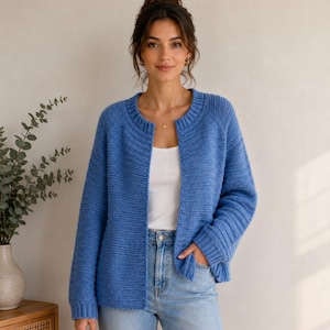 Puede incluir: Un cárdigan de punto azul de manga larga con cuello redondo acanalado y puños acanalados. La prenda presenta un patrón de punto horizontal texturizado, un diseño frontal abierto y un dobladillo recto, usado sobre una camiseta blanca y jeans azules.