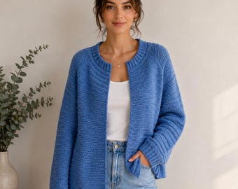 May include: A blue long-sleeved knit cardigan with a ribbed crew neckline and ribbed cuffs. The garment features a textured horizontal stitch pattern, an open front design, and a straight hemline, worn over a plain white top and light blue denim jeans.