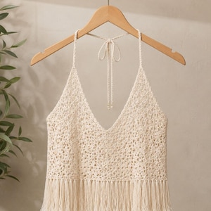 Peut inclure: Un haut dos nu en crochet de couleur crème présentant un motif ajouré complexe, une encolure en V profonde et de fines bretelles tressées qui se nouent dans le dos. L'ourlet inférieur est orné d'une longue frange droite sous la taille.