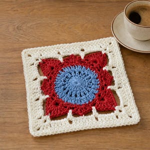 May include: A square crochet coaster featuring a central light blue circular motif surrounded by a red floral-inspired pattern, all framed by an off-white border with openwork details. The coaster is crafted with intricate yarn stitching.