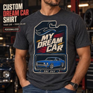 Könnte beinhalten: Ein dunkelgraues Kurzarm-T-Shirt mit einem Grafikdruck eines blauen Oldtimers in einem stilisierten Verpackungsdesign. Der Text lautet "MY DREAM CAR" und "ONE DAY" mit roten und gelben Akzenten. Das Shirt hat einen Rundhalsausschnitt und eine melierte Textur.