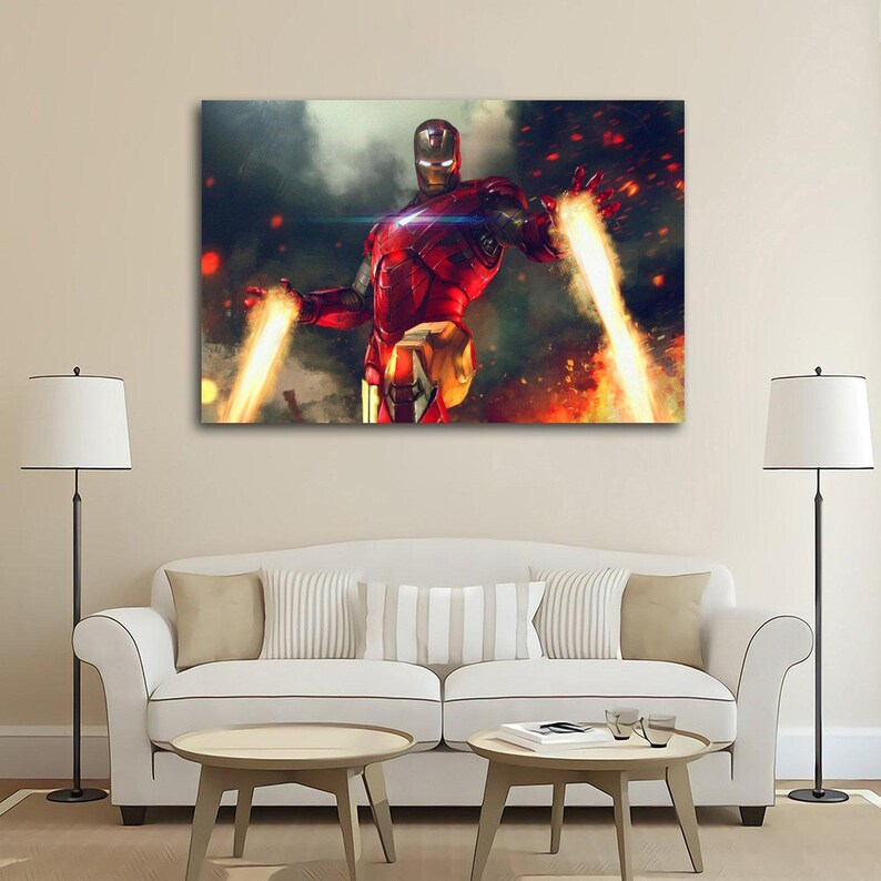 May include: A canvas print of Iron Man in a dynamic pose, with his arms extended and repulsor rays blasting outwards. The artwork features a red and gold armored suit against a fiery, smoky background. The image is displayed above a white sofa.