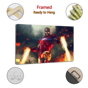 May include: Framed canvas art featuring Iron Man in a dynamic pose, with bright energy beams emanating from his hands. The artwork is predominantly red and gold, set against a smoky, fiery background. Text at the top reads "Framed Ready to Hang."