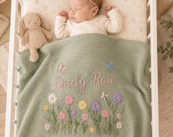 Könnte beinhalten: Ein schlafendes Baby in einem Kinderbett, bedeckt mit einer salbeigrünen Strickdecke. Die Decke ist mit bunten Blumen, Schmetterlingen und dem Namen "Emily Rose" bestickt. Ein Stofftier-Hase liegt neben dem Baby.
