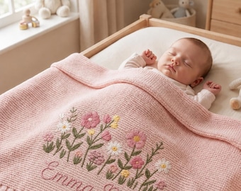 Könnte beinhalten: Ein schlafendes Baby liegt unter einer rosa Strickdecke. Die Decke ist mit einem floralen Design und dem Namen "Emma Rose" bestickt. Das Kinderbett ist aus hellem Holz gefertigt, und ein Teddybär sitzt auf der Fensterbank.