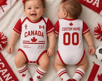 Könnte beinhalten: Zwei weiß-rote Baby-Bodys mit Kanada-Motiven. Die Vorderseite zeigt das Wort CANADA, ein Ahornblatt, ein Pokalsymbol und den Text TRUE NORTH STRONG AND FREE. Die Rückseite ist mit CUSTOM NAME und der Nummer 00 sowie einem Ahornblatt bedruckt.