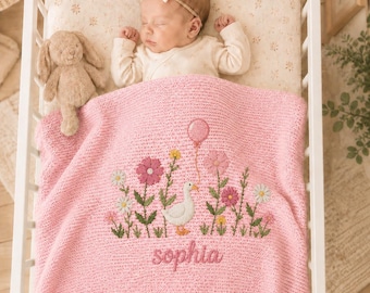 Könnte beinhalten: Ein schlafendes Baby in einem Kinderbett, bedeckt mit einer rosa Strickdecke. Die Decke zeigt gestickte Blumen, eine Gans und den Namen "Sophia". Ein Stoffhase liegt neben dem Baby.