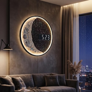 Könnte beinhalten: Eine kreisförmige Wanduhr mit einem texturierten Mondsichel-Design auf einem dunklen, sternenklaren Hintergrund, einem leuchtenden Rand und einer Digitalanzeige, die die Zahlen 5 23 zeigt. Die Uhr ist an einer dunkelgrauen Wand über einem Sofa montiert.