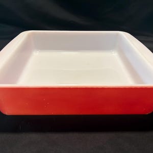 Puede incluir: Una fuente de horno cuadrada roja y blanca. El exterior es de un rojo vibrante, mientras que el interior es blanco. La fuente tiene un diseño simple y clásico, perfecto para hornear y servir. Un artículo de cocina versátil.