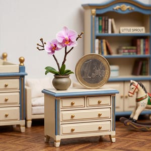May include: A miniature cream-colored chest of drawers with blue trim and gold knobs, holding a small potted orchid with pink flowers. A one Euro coin stands next to the chest. A miniature bookshelf and rocking horse are in the background.