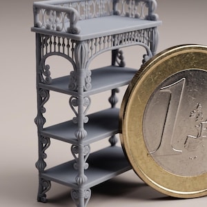 Może przedstawiać: Miniaturowa, szara, dekoracyjna półka z czterema poziomami. Półka ma ozdobne detale, w tym ornamenty i balustradę. Obok półki znajduje się moneta euro dla skali.