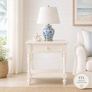 May include: A cream-colored wooden side table with one drawer and a lower shelf, featuring turned legs. On top sits a table lamp with a white fabric shade and a blue and white floral patterned ceramic base, accompanied by a white starfish ornament.