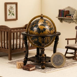 May include: A miniature antique-style globe on a dark wooden stand. The globe features a map design in black and gold. A one Euro coin is next to the globe. A small wooden crib, a small book, and a wooden block with the letter "A" are also in the image.