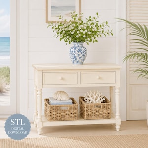 Op de afbeelding: Een crèmekleurige sidetable met twee lades en een onderste plank. Bovenop staat een blauw-witte keramische vaas gevuld met witte bloemen. Op de onderste plank staan twee gevlochten manden, één met een zeeschelp en één met wit koraal.