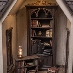 May include: Miniature library scene with a large dark brown bookcase filled with books. A small table with books and a lamp sits in front of the bookcase. The scene is lit by a hanging light and a small oil lamp.