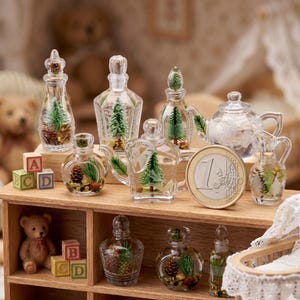 Puede incluir: Colección de botellas y tazas de té de vidrio en miniatura, algunas con decoraciones de pinos y piñas. También hay una moneda de un euro. Los artículos se exhiben en una estantería de madera con un oso de peluche y bloques de alfabeto.