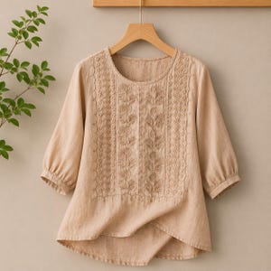 May include: A beige blouse with three-quarter length sleeves and a round neckline. The front panel features vertical bands of intricate tonal embroidery with floral and geometric patterns, finished with a scalloped edge along the neckline.