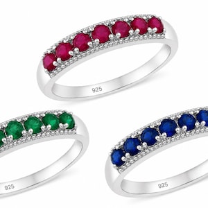 Può includere: Tre anelli in argento con il marchio 925 stampato sulla fascia interna. Ogni anello presenta una fila di cinque pietre preziose a taglio rotondo di colore rosso, verde e blu, incastonate in un canale d'argento lucido con bordi decorativi.