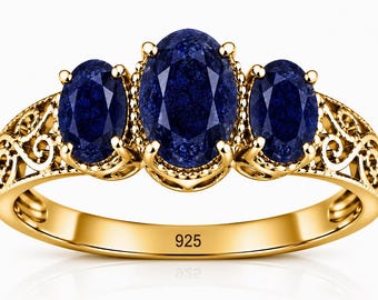 May include: A gold-toned ring featuring three oval-cut dark blue stones set in a filigree band. The central stone is larger than the two flanking stones. The inner band is clearly stamped with the number 925, indicating sterling silver composition.