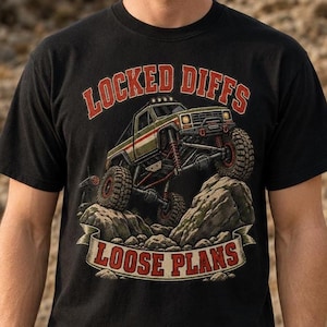 May include: A black short-sleeve t-shirt featuring a graphic of an olive green off-road truck climbing over rocks. The text "LOCKED DIFFS" appears in red above the truck, and "LOOSE PLANS" is printed in red on a banner below the rocks.