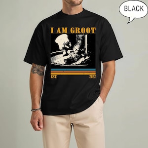 May include: Black t-shirt with a graphic featuring the phrase "I AM GROOT" in yellow block letters above a black and white image of Groot as a chef. Below the image are horizontal stripes and the text "EST. 2022".