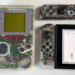 May include: Transparent Nintendo Game Boy and Switch controllers, revealing internal circuits. The Game Boy features a grey screen and the text "Nintendo GAME BOY". The Switch controllers are connected to a black screen showing controller settings.
