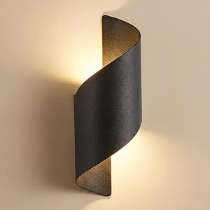 Peut inclure: Une applique murale noir mat avec un design métallique incurvé en forme de S. Le luminaire présente une structure ouverte permettant à une lumière chaude et douce de s'échapper par les ouvertures supérieure et inférieure, créant un éclat.
