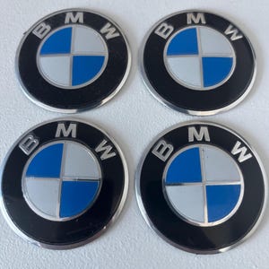 以下が含まれることがあります： 4つの円形BMWエンブレム。各エンブレムは、シルバーの文字「B」、「M」、および「W」が付いた黒い外側のリングを備えています。各エンブレムの中央には、青とシルバーの4象限デザインがあります。