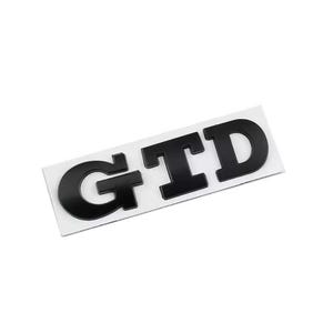 May include: Black GTD badge on a white rectangular backing. The letters are bold and in a sans-serif font. The badge is likely for a vehicle.