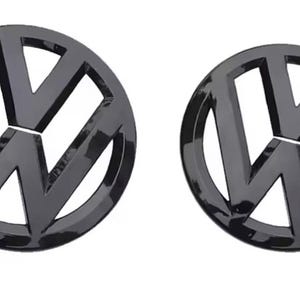 May include: Two glossy black Volkswagen emblems. Each emblem features the iconic VW logo, a stylized 'V' and 'W' within a circle. The emblems are circular and have a reflective, shiny surface, suggesting a car accessory.