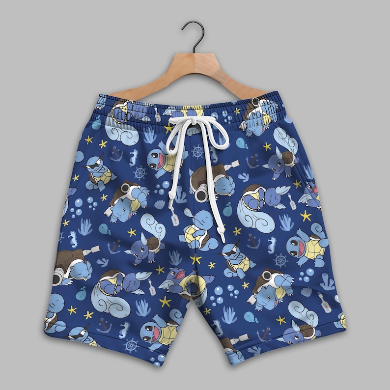 K&ouml;nnte beinhalten: Blaue Shorts mit einem durchgehenden Muster aus hellblauen, schildkr&ouml;tenartigen Wesen, gelben Seesternen, Ankern, Steuerr&auml;dern und kleinen wei&szlig;en Blasen. Die Shorts haben einen elastischen Bund mit wei&szlig;en Kordelz&uuml;gen und h&auml;ngen an einem Holzb&uuml;gel.