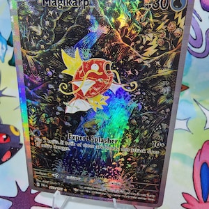 May include: A holographic Magikarp Pokémon trading card. The card features a red and white Magikarp illustration with the text "Expert Splasher". The card has a holographic background with a 30 HP rating.