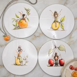 May include: Four round white ceramic plates featuring watercolour-style illustrations of small winged fairies perched on fruit. One plate shows a fairy on an orange, one on a lemon, one on a pear, and one between two cherries. A matching orange pendant is included.