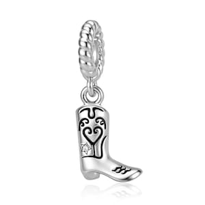 Può includere: Un ciondolo in argento a forma di stivale da cowboy con dettagli in smalto nero a forma di cuore e volute, impreziosito da una piccola pietra trasparente a forma di stella incastonata sul lato, sospeso a un occhiello circolare ritorto.