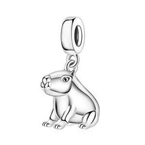 May include: A polished silver charm in the shape of a capybara, featuring a smooth, reflective surface and a rounded bail at the top for attachment to a bracelet or necklace chain. The animal figure is depicted in a seated, side-profile position.