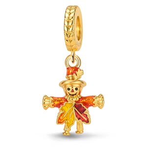 May include: A gold-toned charm featuring a scarecrow figure with a hat and a body made of autumn leaves in shades of yellow, orange, and red. The charm includes a circular bail with a textured wheat-like pattern along the outer edge.
