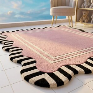 May include: A pink rectangular rug with a scalloped edge and a black and white striped border. The rug has a white border and is placed on a tiled floor. A chair and shelf with teddy bears are in the background.