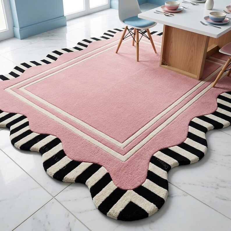 May include: A pink rug with a scalloped edge and a rectangular center. The rug has a white border and a black and white striped pattern on the edge. The rug is on a white tile floor.