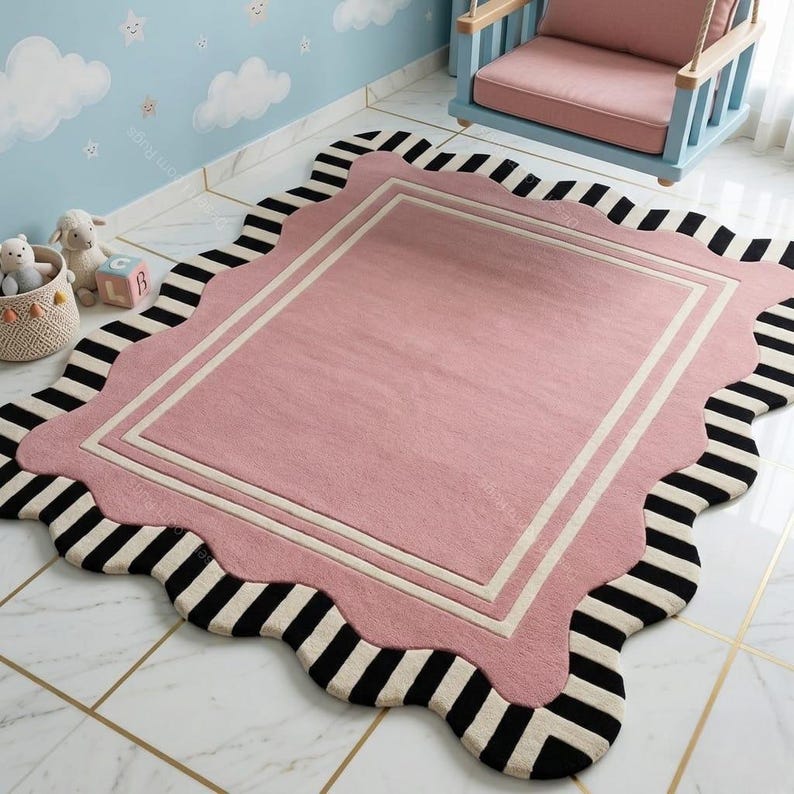 May include: A pink rectangular rug with a scalloped edge and a black and white striped border. The rug has a white border and is placed on a tiled floor. A blue and pink swing chair is in the background.