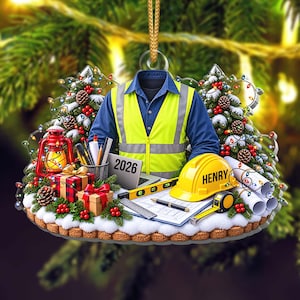 Könnte beinhalten: Ein Weihnachtsschmuck mit einem blauen Hemd und einer gelben Warnweste, einem gelben Schutzhelm mit der Aufschrift HENRY, einem Laptop mit 2026, einer roten Laterne, Geschenken, Bauplänen, einer Wasserwaage, einem Maßband und Stiften.