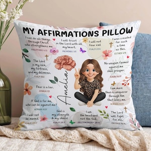 Puede incluir: Cojín cuadrado blanco con el texto "MY AFFIRMATIONS PILLOW" y citas inspiradoras. El cojín presenta una ilustración de dibujos animados de una niña, detalles florales y el nombre "Amelia".