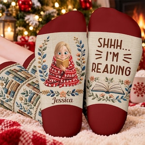 May include: A pair of socks with a cream-colored base and deep red cuffs. One sock features a cartoon character wrapped in a red blanket reading a book, with the name Jessica below. The other sock displays the text SHHH... I'M READING above an open book graphic.