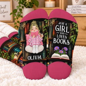 May include: A pair of pink and black socks featuring a graphic of a person reading a book in front of a bookshelf. The text reads Just a Girl Who Loves Books and the name Olivia. The design includes a book with purple flowers and greenery.