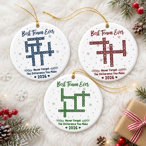 Peut inclure: Trois ornements ronds en céramique blanche avec des cordons dorés. Chaque pièce présente un motif de mots croisés avec des prénoms, le texte "Best Team Ever", "Never Forget The Difference You Make" et "2026" en bleu, rouge ou vert avec des flocons.