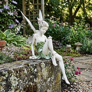 Könnte beinhalten: Eine weiße und grüne Feenstatue mit detaillierten Flügeln und einem fließenden Kleid, die auf einer Steinmauer sitzt. Die Fee ist von üppigem Grün umgeben, darunter Blumen und Pflanzen, was eine ruhige Gartenszene schafft.